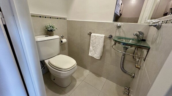A bathroom with a toilet, a glass sink, and a towel rack.