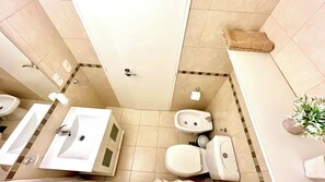 A bathroom with two sinks, a toilet, and a bidet. There is a towel rack and a plant on the wall.