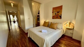 A hotel room with a bed, a bedside lamp, a painting on the wall, and a view of the hallway.