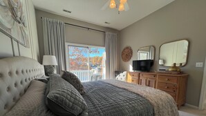Une chambre à coucher avec un grand lit, une commode, un téléviseur et une fenêtre avec des rideaux.