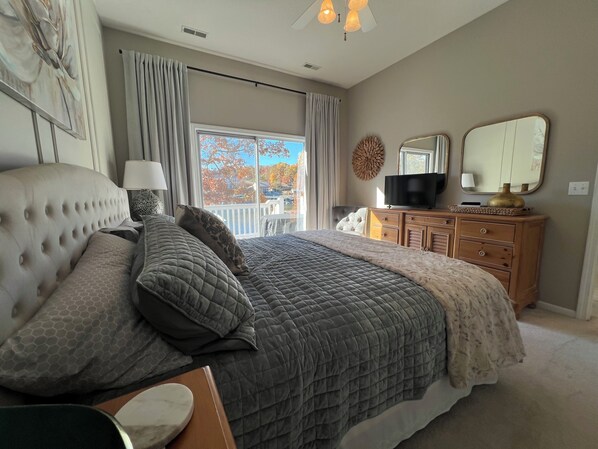 Een slaapkamer met een groot bed, een kaptafel, een televisietoestel en een raam met gordijnen.