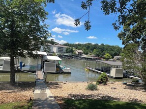 A riverside dock with boats, a covered seating area, and a view of buildings across the water.