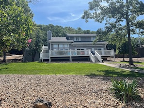 A two-story house with a deck, surrounded by trees and a well-maintained lawn.