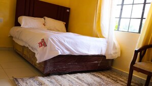 Ein Bett mit hölzernem Kopfteil, weißer Bettdecke und einem gemusterten Teppich auf Fliesenboden.