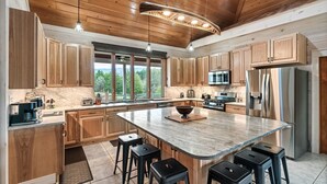 A spacious kitchen with wooden cabinets, a large island with stools, stainless steel appliances, and a view of the outdoors. - Lakefront - Private Resort with INGROUND POOL! (Dandridge)