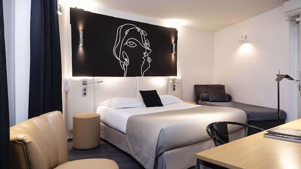 A modern hotel room with a bed, a desk, a chair, a sofa, and a wall-mounted artwork. - Bridgestreet Montparnasse / St Germain (Paris)