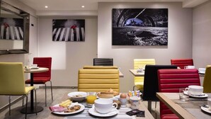A modern dining area with red and yellow upholstered chairs, a table set with breakfast items, and two large black-and-white paintings on the walls. - Bridgestreet Montparnasse / St Germain (Paris)