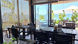 An outdoor dining area with tables and chairs, large windows, and a view of the ocean. - Pandora Beach Mui Ne Retreat (Mui Ne)