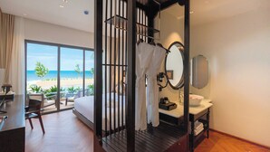 A bedroom with a large window, a bed, a desk, and a bathroom with a sink and mirror. - Pandora Beach Mui Ne Retreat (Mui Ne)