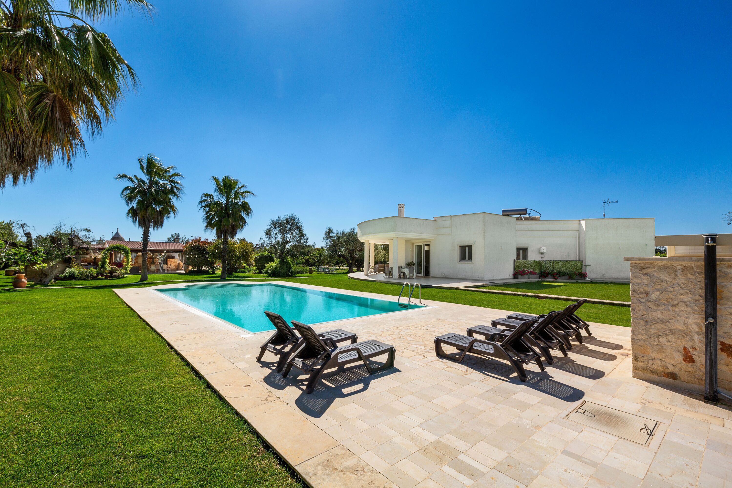 Una piscina con sillones de descanso, un césped cuidado y una casa moderna al fondo.