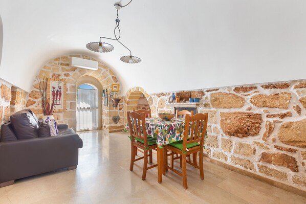 A cozy dining area with a stone wall, a wooden table with chairs, and a sofa in the foreground.