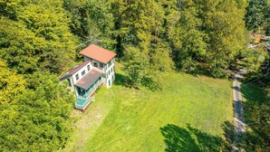 An aerial view of a house surrounded by dense forest, with a clear path leading to the entrance.