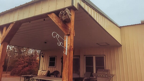 Ein Gebäude mit einer überdachten Veranda, einem Holzmast mit geschnitztem Gesicht und einem Grill auf der Veranda.