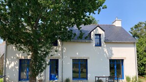 A two-story house with a white exterior and blue accents, including doors and windows. There is a tree in the front yard and a small table with chairs outside. - House near beach, 3 double bedrooms with private bath. View of château. (Sarzeau)
