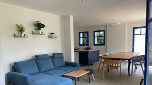 A modern living room with a blue sofa, a wooden dining table, and a kitchen area in the background. - House near beach, 3 double bedrooms with private bath. View of château. (Sarzeau)