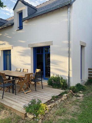 Una casa moderna con una terrazza, un tavolo da pranzo con sedie e una porta blu.