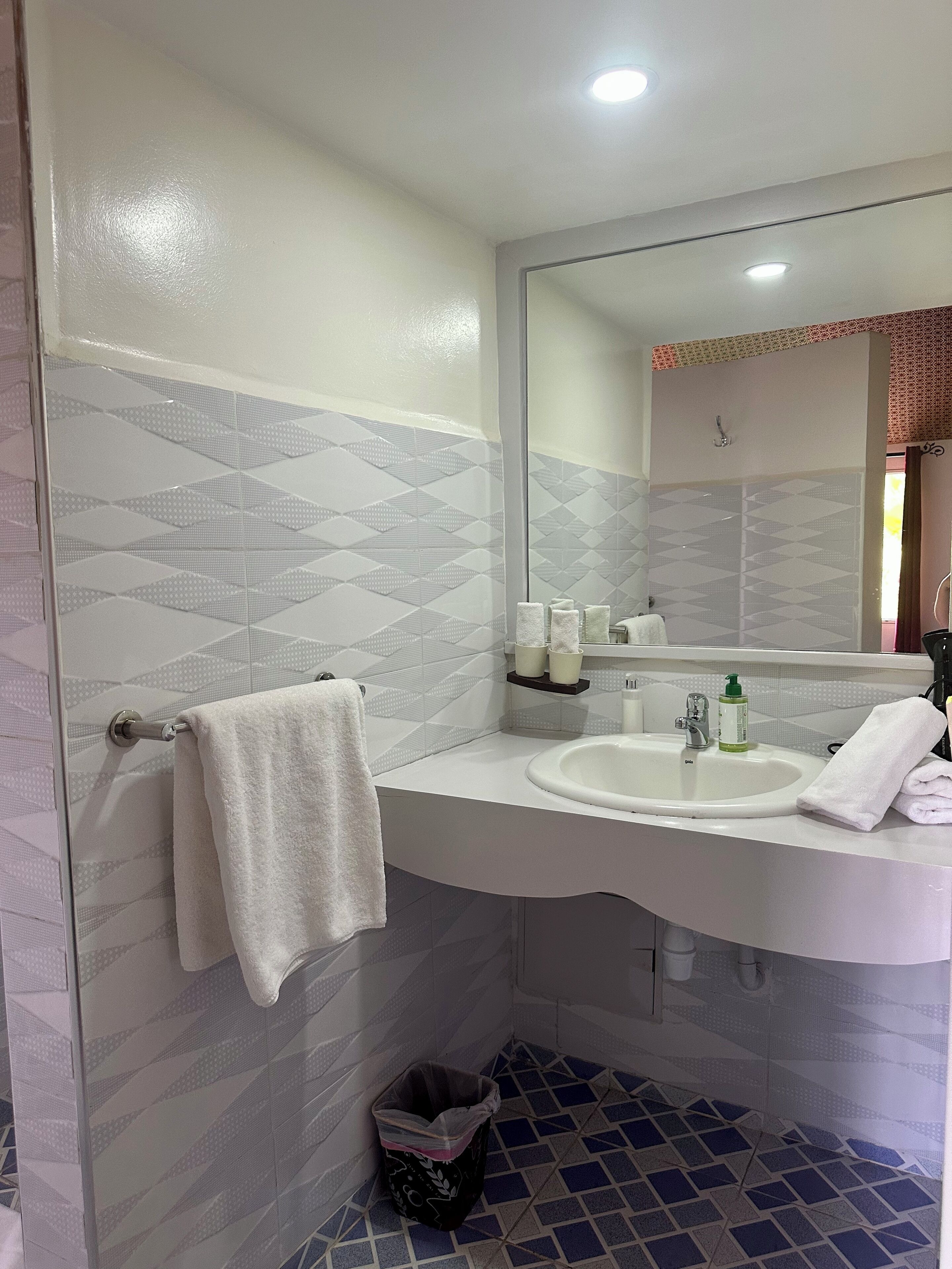 A bathroom with a white sink, a mirror, and patterned tiles on the walls.