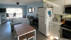 A compact kitchen with white cabinets, a refrigerator, a microwave, and a wooden dining table.