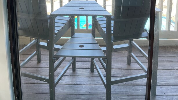 A balcony with two chairs and a table, overlooking a building with multiple balconies and a pool.
