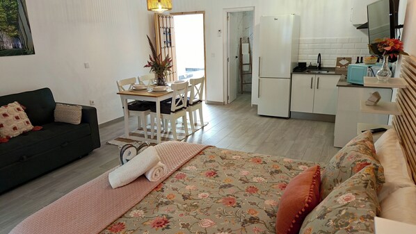 Una sala de estar acogedora con un sofá, una cama con ropa de cama floral y un comedor con una mesa y sillas.