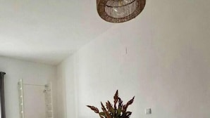A dining area with a wooden table set for four, surrounded by white chairs. A vase with dried plants is on the table, and a woven light fixture hangs above. - Antonio Parra II Tourist Apartments (Jerez de la Frontera)