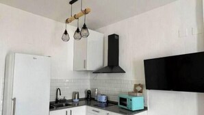 A modern kitchen with white cabinets, a black range hood, a built-in microwave, and a hanging light fixture. - Antonio Parra II Tourist Apartments (Jerez de la Frontera)