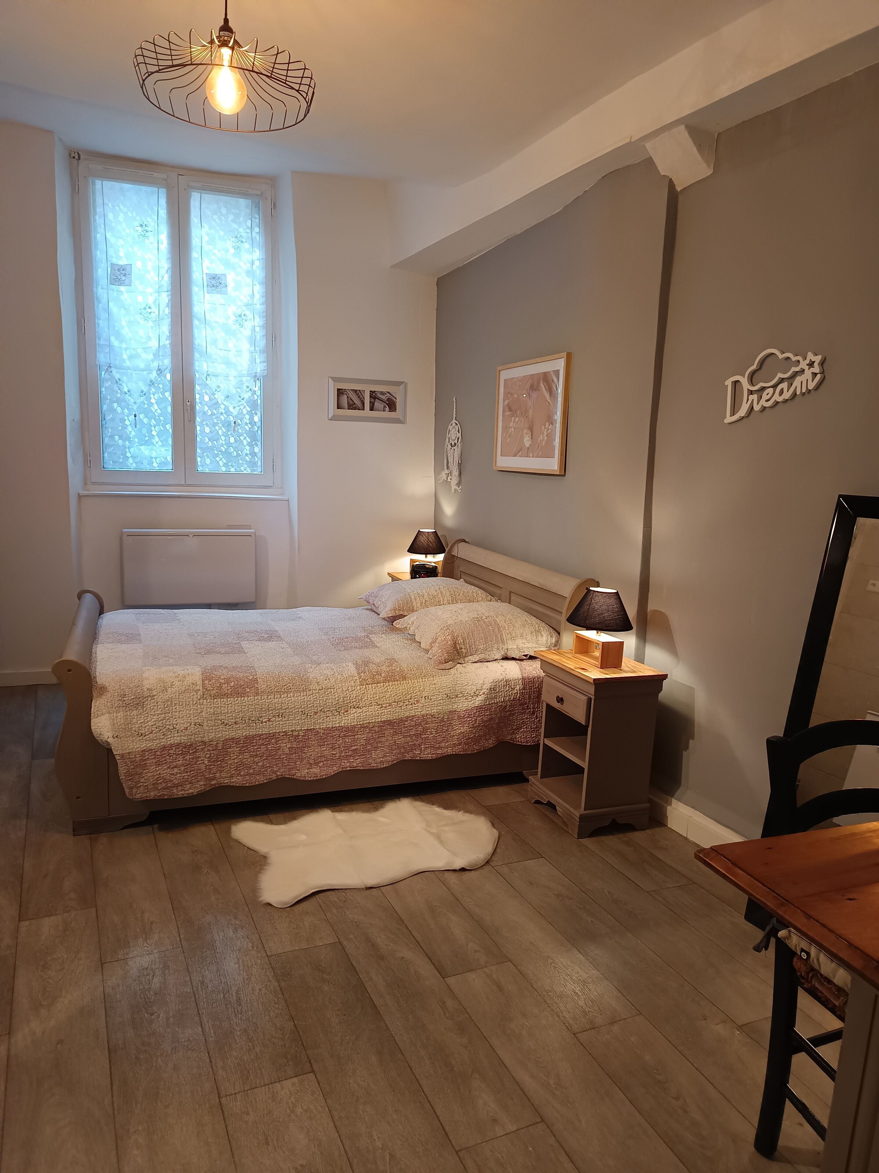 Un dormitorio con cama, mesitas de noche, lámpara, sillón, alfombra y una pared con un letrero que dice 'Dream'.