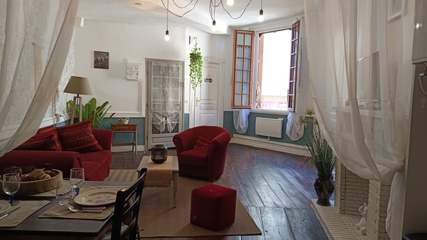 Un salón con zona de comedor, sofás rojos, una mesa de madera y un ventanal con cortinas.