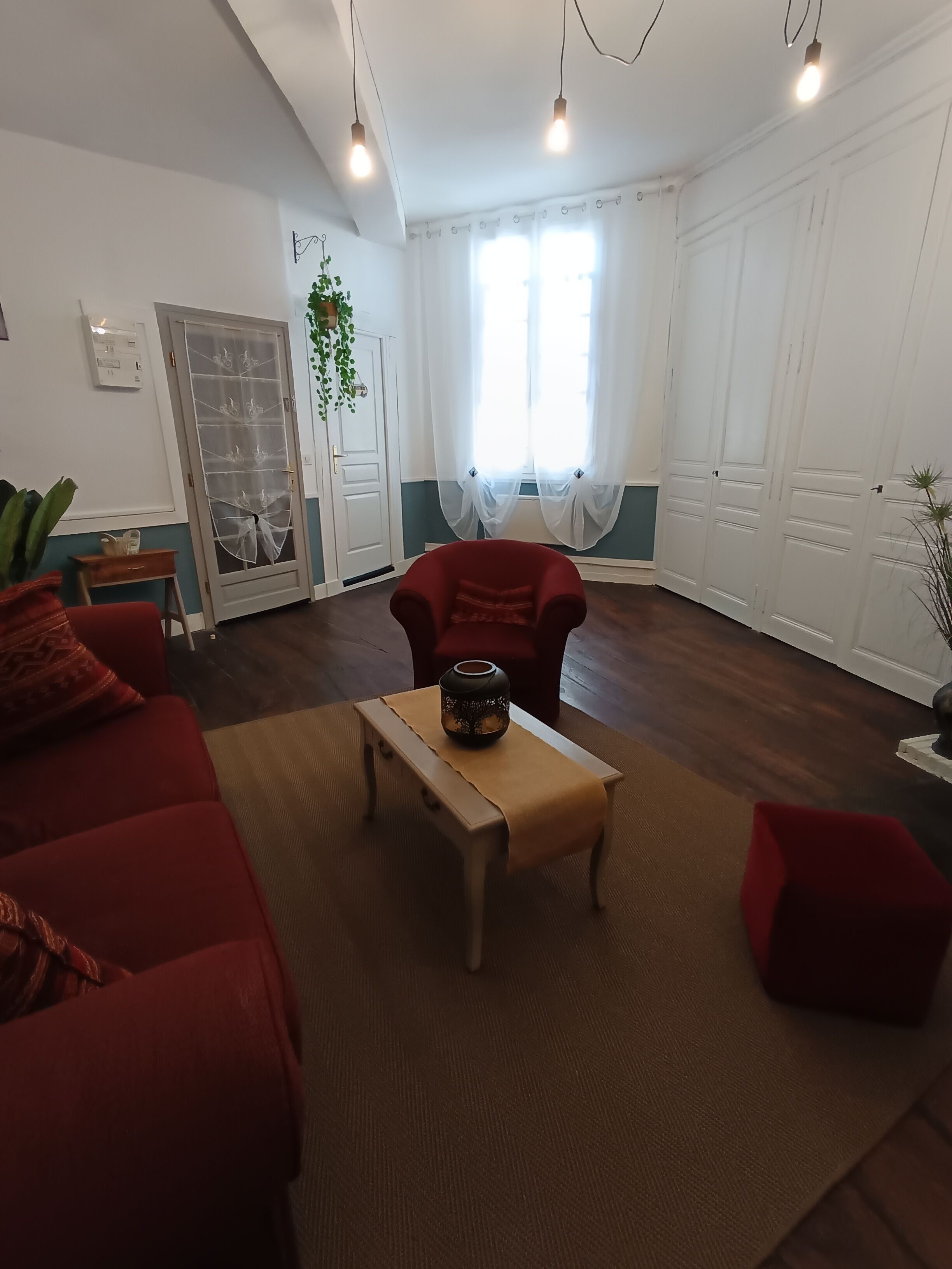 A living room with a red sofa, a wooden coffee table with a decorative item, a red armchair, and a large window with sheer curtains.