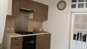 Cocina compacta con armarios de madera, cocina a gas, lavamanos y un reloj en la pared.