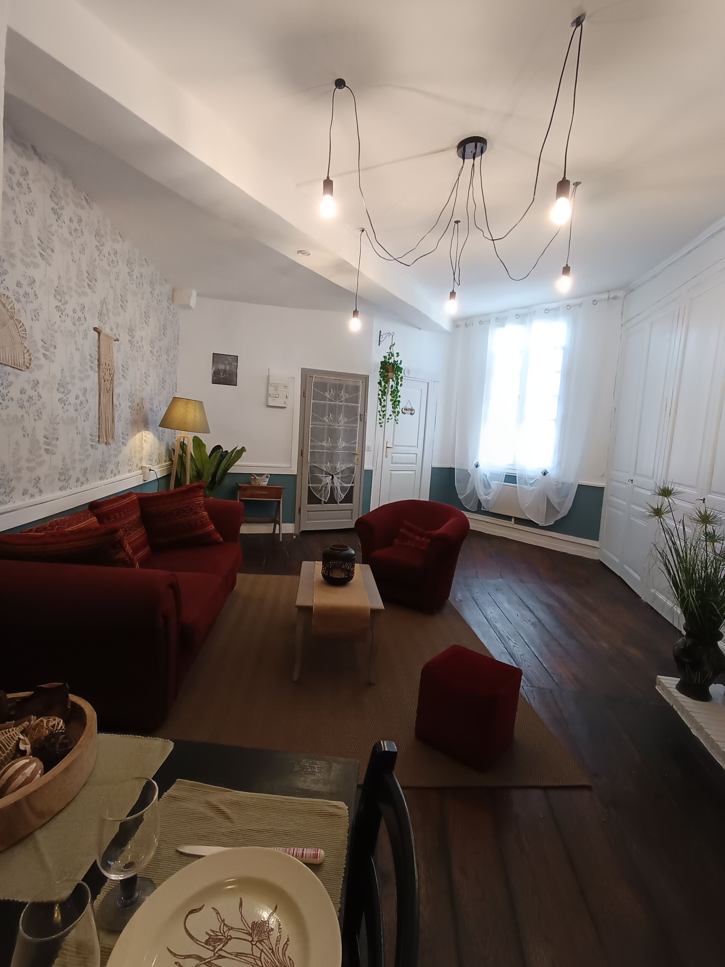 En stue med en rød sofa, et lille bord med en skål og vinglas, samt en rød lænestol.