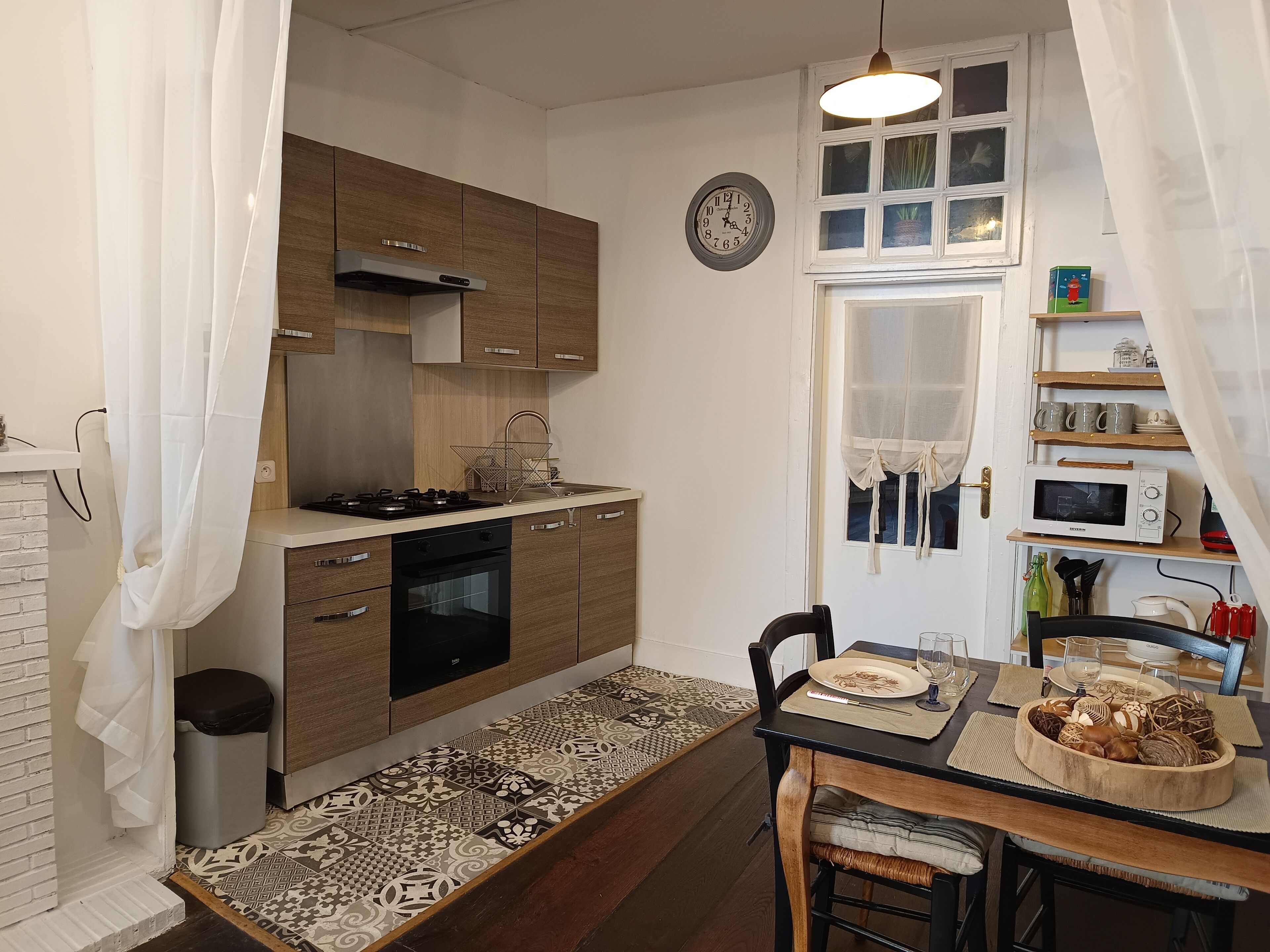 A compact kitchen with wooden cabinets, a built-in oven, a microwave, and a dining area with a table set for two.