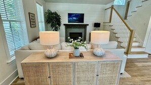 A living room with a sofa, two lamps, a fireplace, and a staircase. - Wharf Street Coastal Escape - 3BR Old Town Luxury (Bluffton)