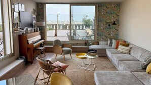 A living room with a piano, a sofa, a dining table, and a large window with a city view. - Exceptional family duplex with breathtaking views of Paris! (Paris)