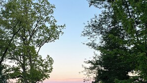 Ein Rasen mit weißen Zäunen, ein großer Baum und ein Blick auf ein Gewässer in der Ferne.