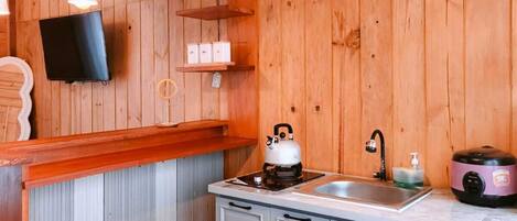 Una cocina compacta con paredes de madera, una encimera blanca y un fregadero. Hay armarios, una tetera y una olla de cocción lenta en la encimera.