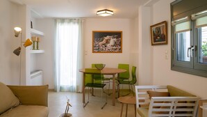 A modern living room with a sofa, a dining table with chairs, a potted plant, and artwork on the walls.