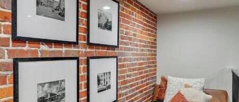 A room with a brick wall, a bed with a white blanket, and four framed pictures.