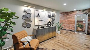 A modern living room with a leather sofa, a wooden floor, a brick wall, and a large mirror.