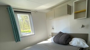 A bedroom with a bed, a window with curtains, a bedside table, and a built-in wardrobe. - Mobile home P007 6 persons (Vendays-Montalivet)