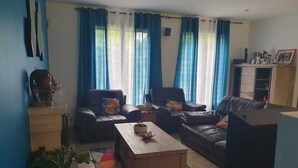 Una sala de estar con un sofá, una mesa de centro y un televisor. Hay cortinas, un armario y una planta.