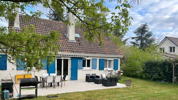 Una casa con techo de tejas, un patio con mobiliario exterior y una parrilla.