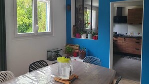 Un comedor con mesa, sillas, una jarras y una ventana con vistas a follaje.