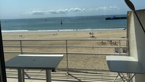 A beach view from a balcony with a table and chairs, a sandy beach, and the sea.