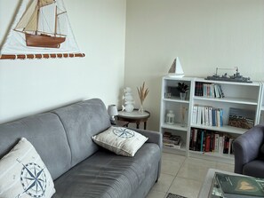 Un salon avec un canapé gris, une bibliothèque et une petite table avec une lampe.