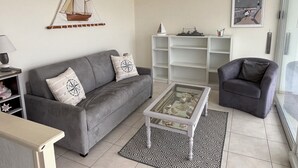 A living room with a grey sofa, a glass coffee table, and a bookshelf.