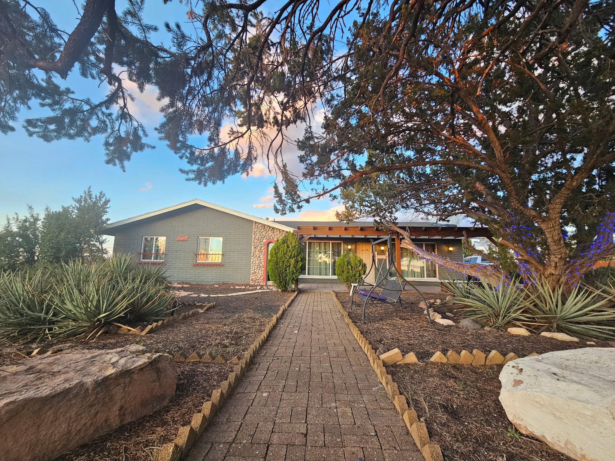 A building with a brick facade, a paved walkway leading to the entrance, and a garden with agave plants.