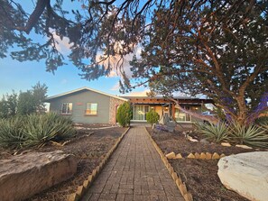 A building with a brick facade, a paved walkway leading to the entrance, and a garden with agave plants. - Najajo Suite #1                                  . (Williams)