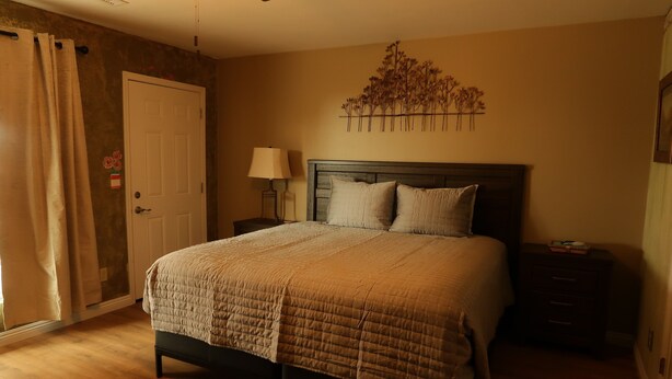 A bedroom with a bed, a nightstand, a lamp, a door, and a wall decoration.
