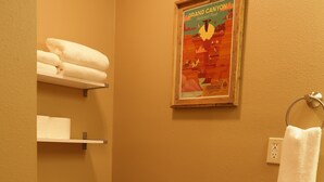 A bathroom with a toilet, a roll of toilet paper, a towel hanging on a rack, and a framed poster on the wall.